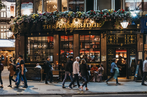 London, United Kingdom - August 31, 2019: Facade of The Cambridge, a traditional pub of unique character next to the Palace Theatre on Charing Cross Road, London, people walking past, in the evening.