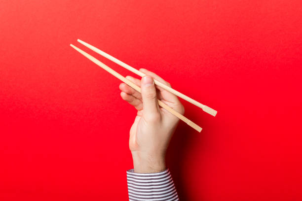 istock Boy's hand showing chopsticks on red background. Asian cuisine concept with empty space for your design 1175055257