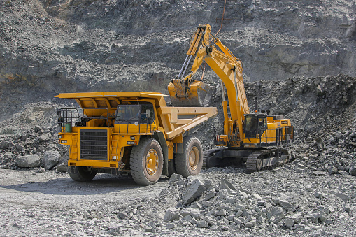 Excavator loads ore into a large mining dump truck. Open pit