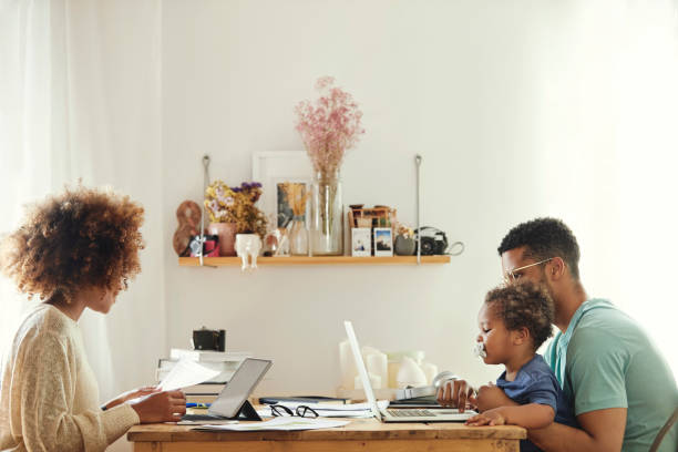 Parents using computer while sitting with boy Mother using digital tablet for working from home. Father using laptop with son at table. They are sitting in kitchen. working at home with children stock pictures, royalty-free photos & images