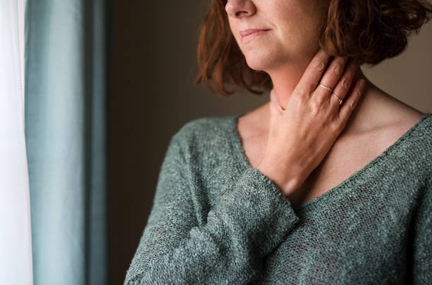 I am not feeling well today Cropped shot of a woman standing by a window with her hand on neck sore throat stock pictures, royalty-free photos & images
