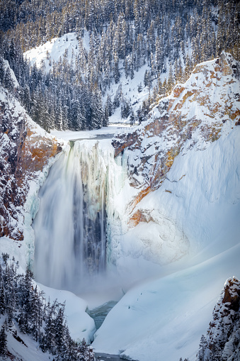 Big Canyon waterfall, partially frozen and surrounded by snow in Yellowstone in winter