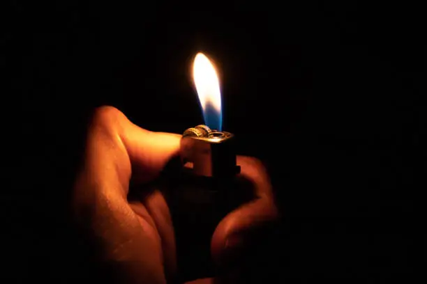 Photo of Hand holding burning gas lighters on dark background