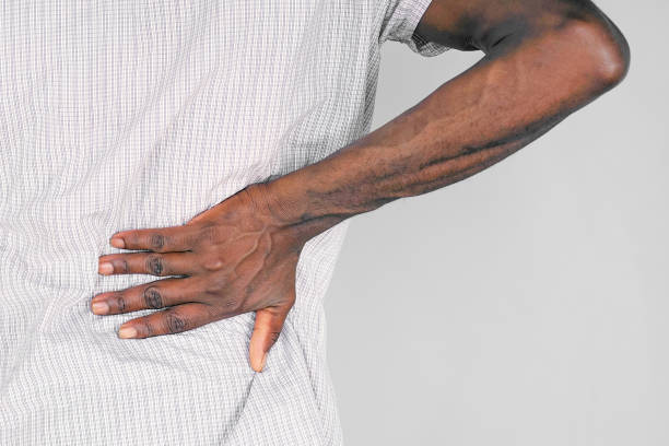 African man, pain at lower back. Close-up view of elderly african man with pain in kidneys isolated on gray background. Elderly african man with back ache clasping her hand to her lower back. African man suffering from ribbing pain, waist pain. chronic illness stock pictures, royalty-free photos & images