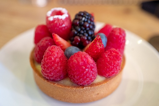 Close-up of a French cuisine pastry or tart, berry flavor, with crust, pasty cream and blueberries and raspberries on a decorate China plate, September 14, 2019
