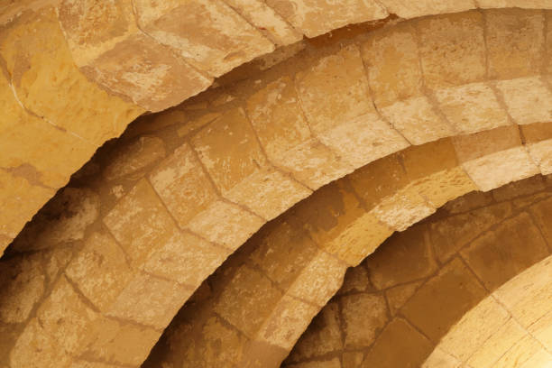 Tightly composed horizontal frame with successive stone block arches curving upward from lower left of frame to upper right.  Single color scheme is golden tan.  The Cittadella - on the Maltese island of Gozo, in the city of Victoria - limestone corridor ceiling.