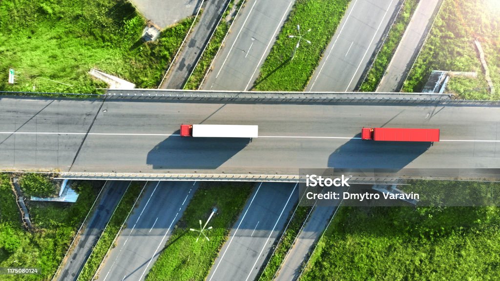 Truck logistics aerial. Two trucks motion by the highway intersection road between fields. View from drone. Truck Stock Photo