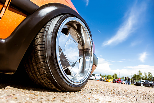 Mirror polished tuned wheels mounted on an understated orange car. Exclusive forged wheels on the pavement against the blue sky.
