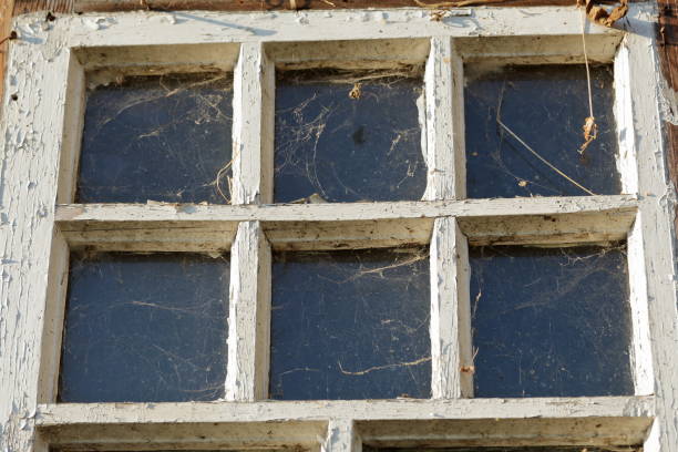 Old window with a wooden frame. Frame with peeling paint. Covered with dust and cobwebs. Dirty glass.