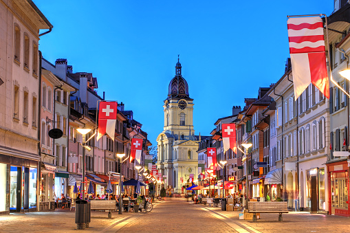 Night scene along the Grand Rue in Morges, Switzerland, with Temple de Morges in the background.