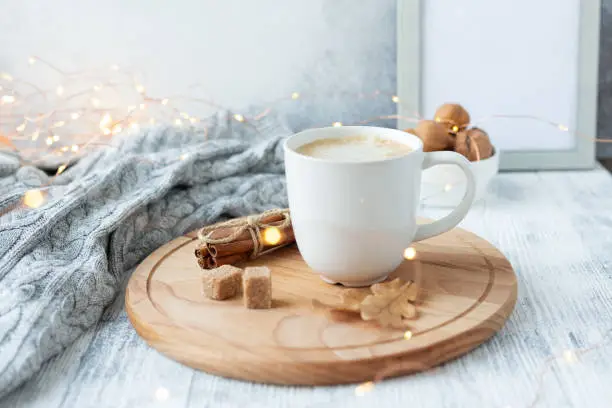 Photo of Coffee mug, sweater, cinnamon, decorated with led lights. Autumn mood. Cozy autumn composition. Hygge concept Soft focus