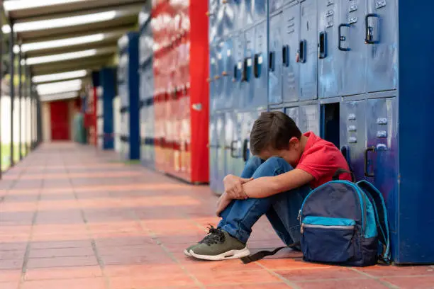 Sad boy at the school sitting on the floor crying about being bullied - lifestyle concepts