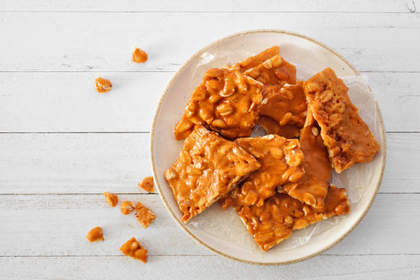 plato de piezas tradicionales de caramelo quebradizo de maní, vista superior sobre madera blanca - taffy fotografías e imágenes de stock