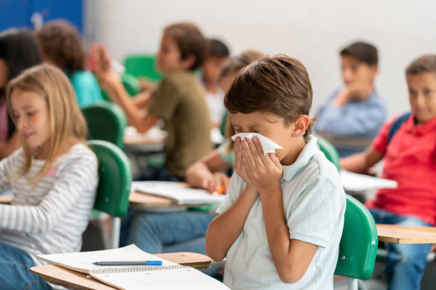 ragazzo malato a scuola che si soffia il naso in classe - condizione medica foto e immagini stock