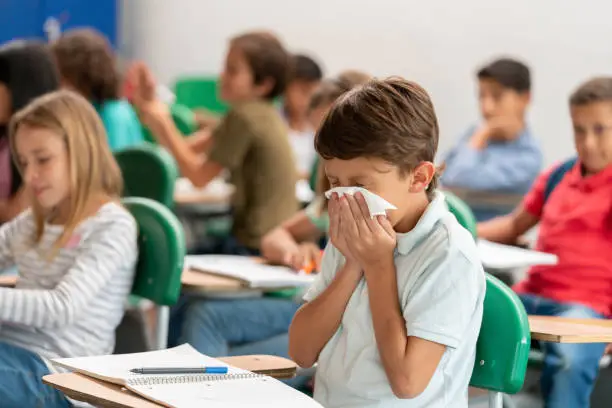 Photo of Sick boy at the school blowing his nose in class