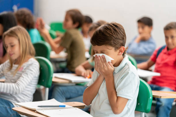 學校裡生病的男孩在課堂上吹鼻子 - 身體健康狀況 個照片及圖片檔