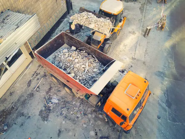 Bulldozer loader uploading waste and debris into dump truck at construction site. building dismantling and construction waste disposal service. Aerial drone industrial background.