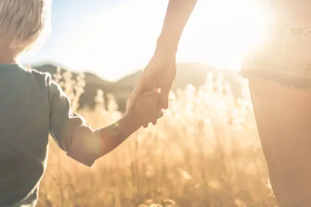 Photo of Mother little child holding hands walking in a grass field at sunset.