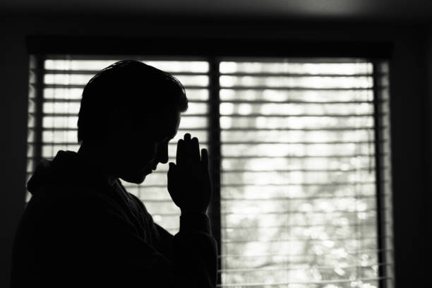 istock Young man saying a prayer next to bedroom window. 1175112233