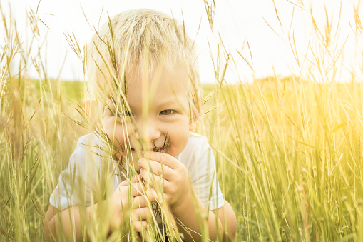 Happy little boy playing outdoors in grass field.
