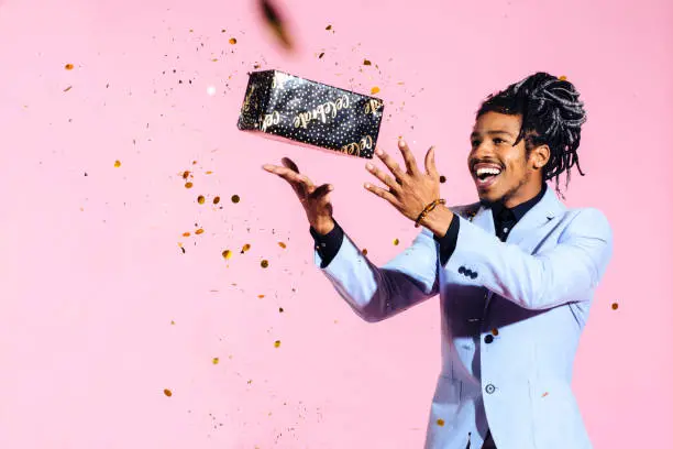 Photo of Excited man throwing gift in the air amid falling gold confetti