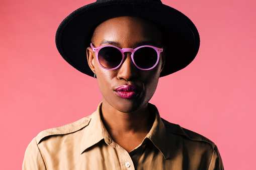 Portrait of a young woman with purple sunglasses, isolated on pink studio background