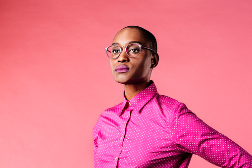 Portrait of a young woman with glasses and pink shirt, isolated on pink studio background