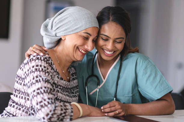 Portrait of an Indian woman with cancer and her doctor Portrait of an Indian woman fighting cancer with her physician. The doctor is a mixed-race female. The two women are seated next to each other indoors. They are embracing and laughing. cancer illness stock pictures, royalty-free photos & images