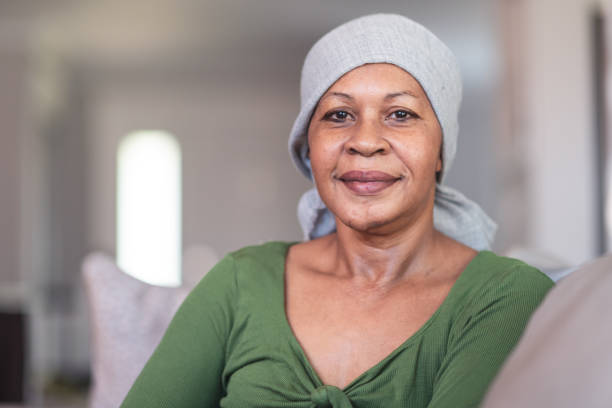 Portrait of a contemplative woman with cancer A mature black woman with cancer is wearing a scarf on her head. She is sitting at home in her living room. She is smiling directly at the camera. She is full of gratitude and hope for recovery. oncology photos stock pictures, royalty-free photos & images