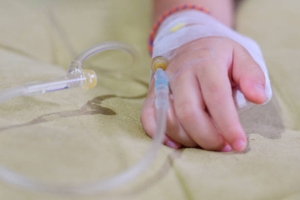 feche acima da infusão iv em uma mão dos pacientes da criança, feche acima da mão do paciente das crianças que recebe a solução salina iv no hostpital - hostpital - fotografias e filmes do acervo