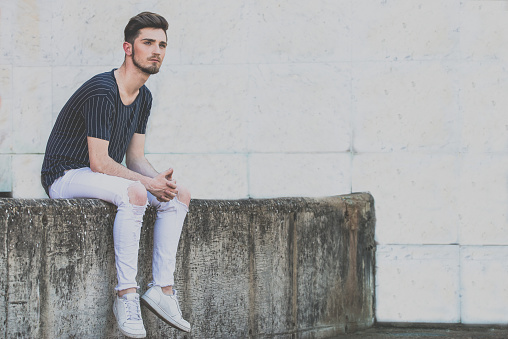 young man sitting on wall and thinking. Pensative guy