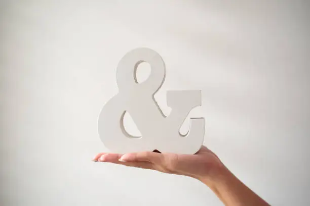 Female hand holding an ampersand in front of white background