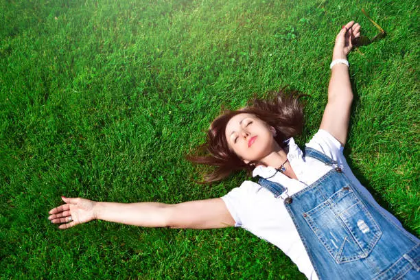 summer-vacation, girl relaxed lying on green grass in an outdoor park. girl in sunglasses enjoying nature lying on grass