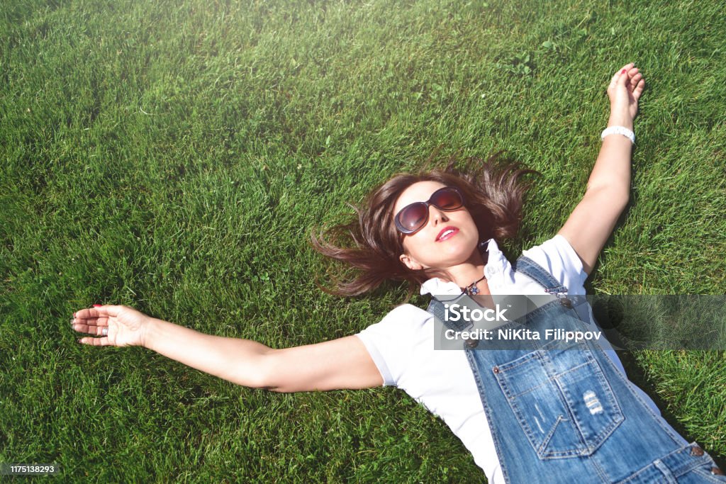 summer-vacation, adult woman relaxed lying on green grass in an outdoor park. girl in sunglasses enjoying nature lying on grass summer-vacation, girl relaxed lying on green grass in an outdoor park. girl in sunglasses enjoying nature lying on grass Adult Stock Photo