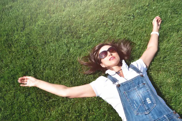 summer-vacation, girl relaxed lying on green grass in an outdoor park. girl in sunglasses enjoying nature lying on grass