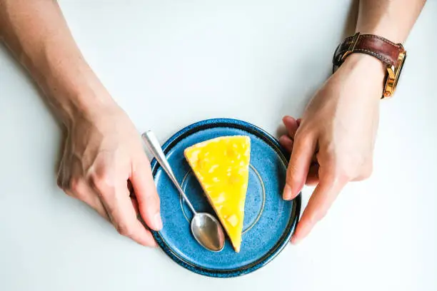 Photo of Top view of woman hands touching a plate with sliced piece of homemade Pineapple cheesecake on isolated white table.