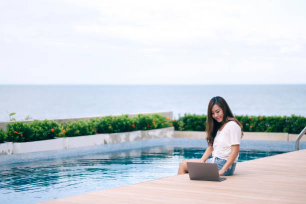 istock woman using and typing on laptop computer while sitting by swimming pool 1175142728