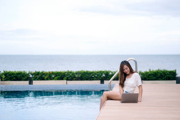 istock woman using and typing on laptop computer while sitting by swimming pool 1175142765