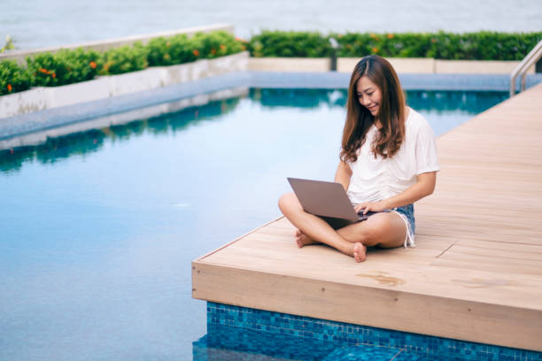 istock woman using and typing on laptop computer while sitting by swimming pool 1175142775