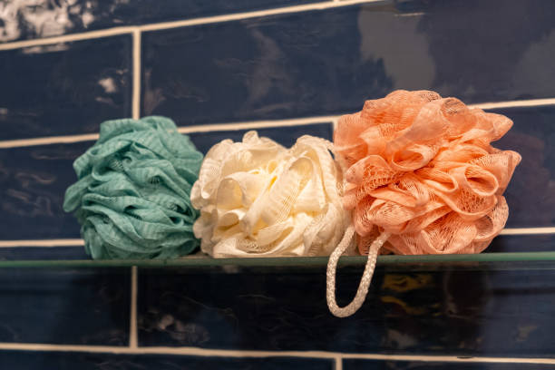 coloridas esponjas de ducha de baño en estante de cristal en el baño - esponja de lufa fotografías e imágenes de stock