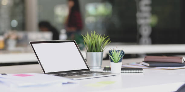 istock Open blank screen laptop with office supplies on white table in modern office 1175149384