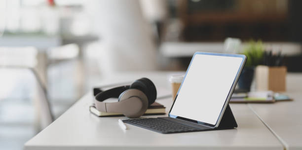 Modern workplace with blank screen tablet, on-ear headphones and office supplies on white table