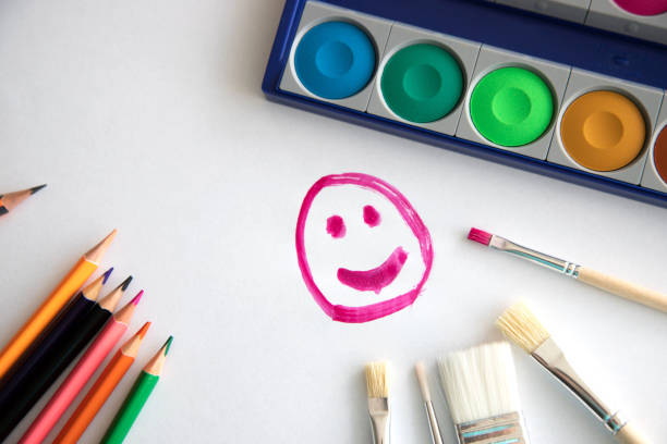 istock happy smile painted with raspberry paint on a white sheet of paper with colored pencils, a box with paint and brushes for painting. The concept of classes with children. Drawing with children 1175166352