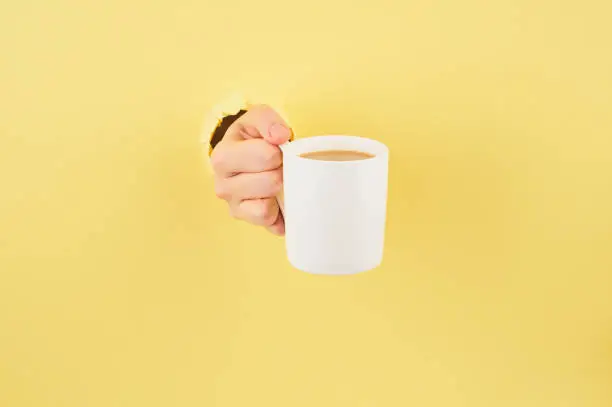 Photo of Unrecognizable person holding a cup of tea on yellow background, copy space closeup