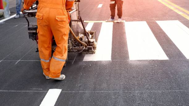 Road worker painting crosswalk on asphalt road