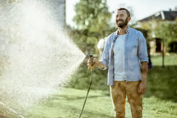 Photo of Man watering green lawn on the backyard