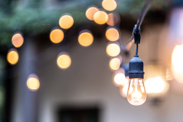 Hanging Outdoor Lights Over Patio With Copy Space One outdoor lightbulb in the foreground is in focus with the rest in the background illuminating with the bokeh effect. The lights are hanging on one single string of lights. patio cover stock pictures, royalty-free photos & images