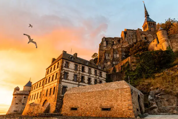 Seagulls flying over dramatic sunset in Mont Saint-Michel.
