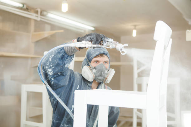 Man painting chair into white paint in respiratory mask. Application of flame retardant ensuring fire protection, airless spraying. Man painting chair into white paint in respiratory mask. Application of flame retardant ensuring fire protection, airless spraying device. airless stock pictures, royalty-free photos & images