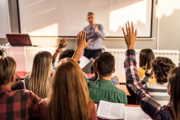 istock Back view of students raising hands on a class at lecture hall. 1175176244